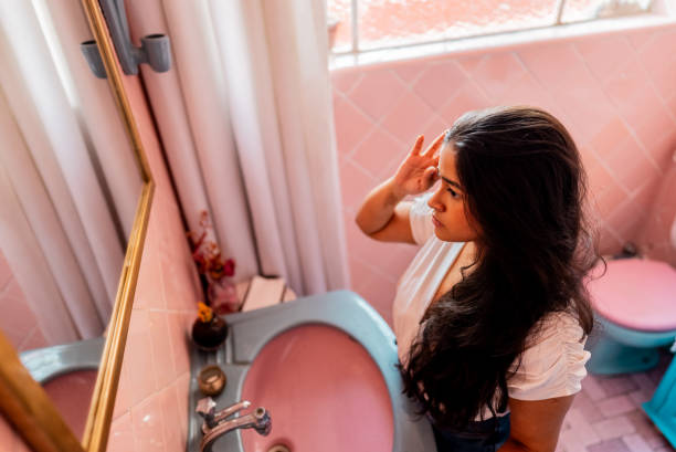 istock Young woman looking at herself in bathroom mirror at home 2204547190