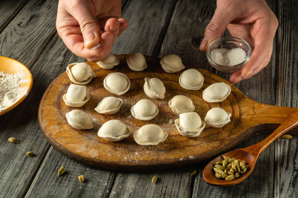 istock Hands skillfully prepare traditional dumplings on a wooden board, surrounded by flour and spices. The kitchen has a warm and inviting atmosphere, showcasing culinary artistry 2204548049