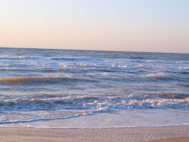 Surf on the beach early in the morning. Big waves, foam and sunrise on the coast. Noise and peace.