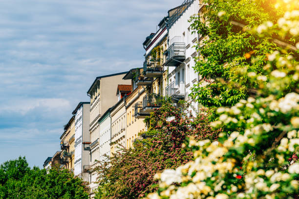 City view showcasing vivid residential architecture alongside blossoming trees on a sunny day in Berlin, Germany. A harmonious blend of historic building facades and vibrant greenery under scattered clouds.
