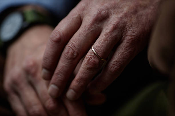 istock Holding Elderly Hand with Wedding Ring Against Dark Background 2204551261