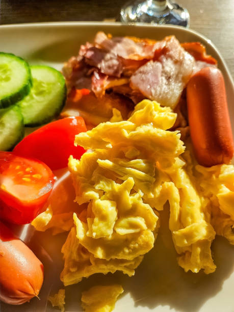 istock Scrambled Eggs, Crispy Bacon, Sausages, and Fresh Vegetables on White Plate 2204551769