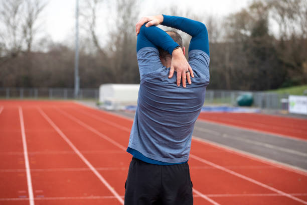 istock Mature male athlete doing a stretch exercise on a running track viewed from behind 2204553954