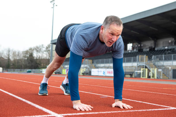 istock Mature male athlete doing a stretch exercise with hands and feet on a running track 2204554016
