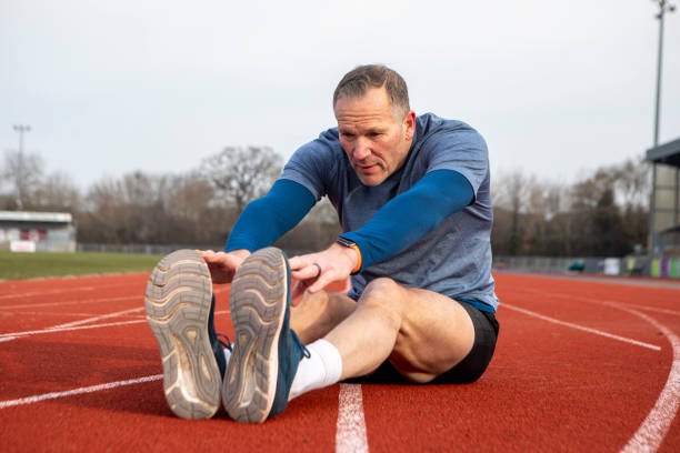 istock Mature male athlete sitting on a running track doing a stretch exercise 2204554094