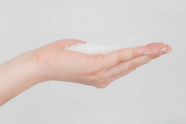 Hand is holding salt crystals to camera in front of white background.
