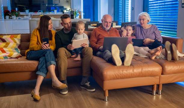 istock Multigenerational Family Sitting On Sofa Absorbed In Digital Devices 2204556530