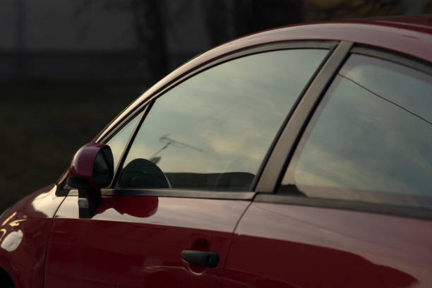 This image is a closeup view of a striking red car, showcasing a beautiful reflection of the vibrant sky in its window, enhancing its appeal