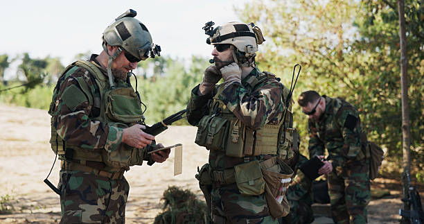 istock Army soldiers in full gear plan a surprise attack, entering tactical data into the system, preparing equipment, and discussing strategy at the training ground in camouflage uniforms and helmets. 2204573034