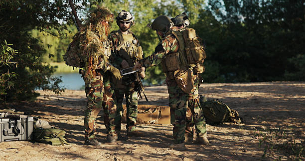 istock A gathering of territorial defense forces at the base, setting up tactics, while the commander in grass camouflage reviews the area's topography on a computer and outlines the plan of action. 2204573635