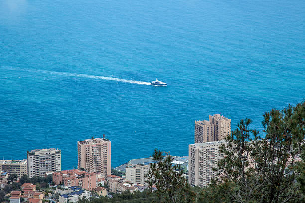 A Monaco city with a beautiful blue ocean in the background. A boat is sailing in the ocean. The city is full of tall buildings