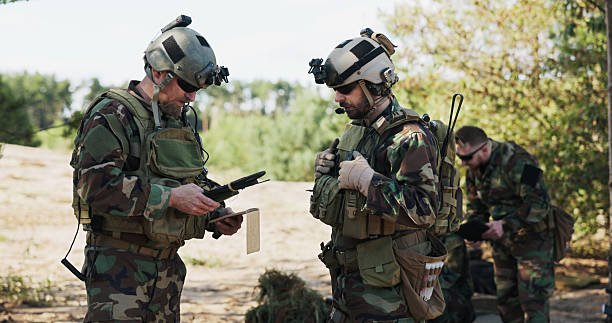 istock Soldiers from an elite military unit plan battle tactics, analyzing data, talking strategy, and preparing equipment at the training ground, dressed in camouflage and helmets. 2204575717