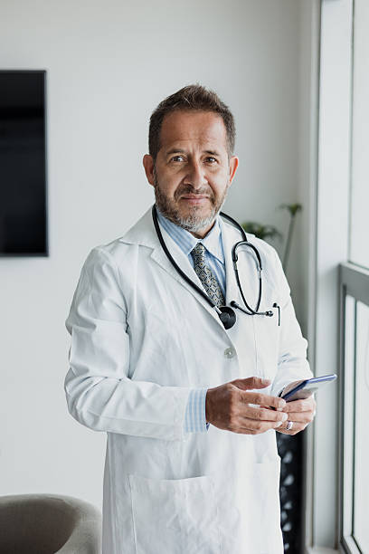 portrait of senior latin man doctor using phone at office or hospital in Mexico Latin America stock photo