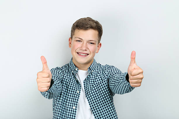 istock Young man with dental braces showing thumbs up on grey background 2204576336
