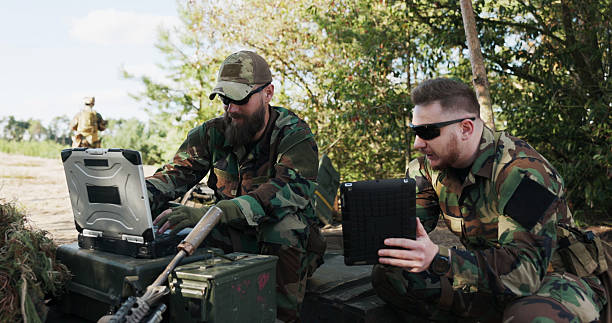 istock A powerful military unit in camouflage and helmets prepares for battle, reviewing data on a tablet, entering tactical information, and discussing a strategy at the training ground. 2204578812