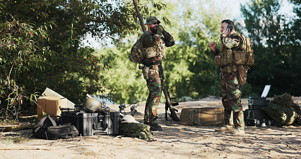 istock Two soldiers in camouflage uniforms prepare for field exercises, securing heavy backpacks, ammo, and weapon belts, ready for a territorial defense mission near the base in the bushes. 2204579317