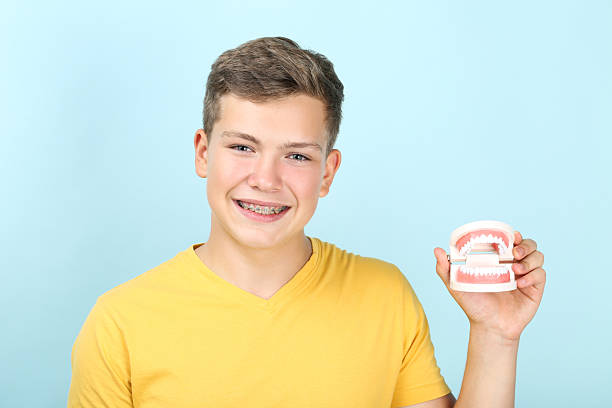 istock Young man with dental braces holding teeth model on blue background 2204579388