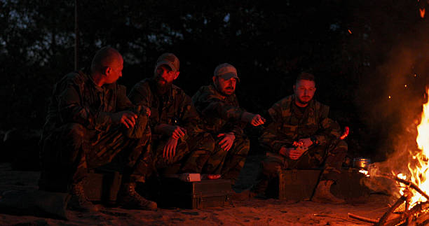 istock Soldiers establish a nighttime camp in the training area, standing around a fire for warmth, roasting sausages, and chatting while remaining on duty to guard the perimeter. 2204581245