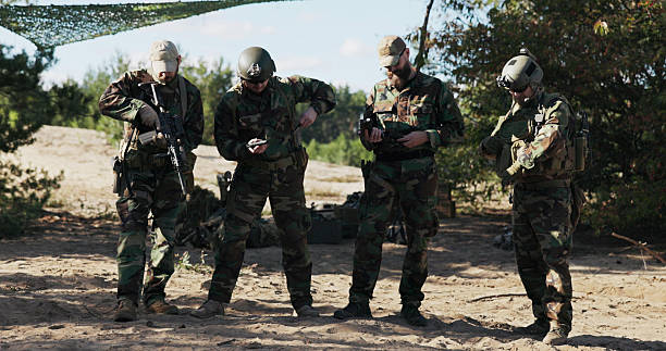 istock Four soldiers in camouflage uniforms stand guard, ready to defend the territory, checking weapons, unlocking pistols and rifles, securing them in holsters and belts. 2204581394