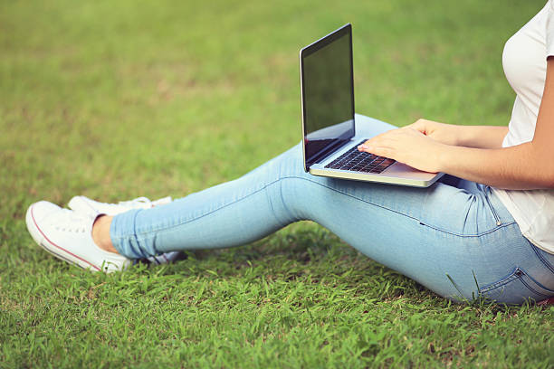 istock Young girl with laptop computer sitting on the grass in park 2204581582