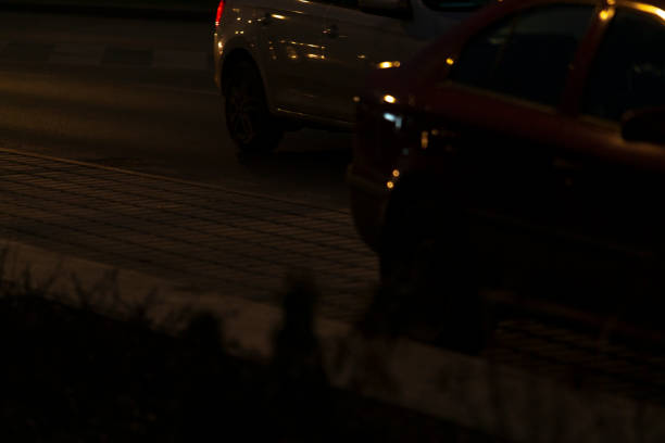 A car is steadily driving down a dark, deserted street in the dead of night, surrounded by shadows and silence