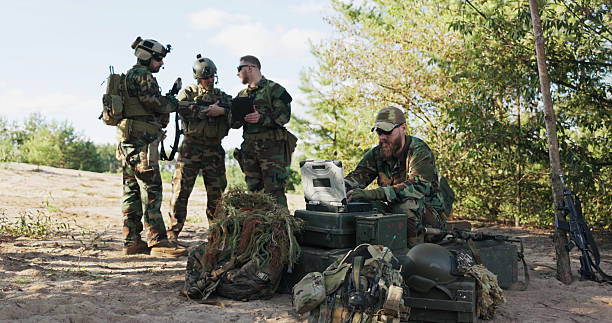 istock Soldiers prepare for deployment, finalizing mission details, securing equipment and clothing for a forest expedition, following maps, entering data, and sending real-time updates to the base. 2204581665