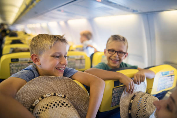 istock Two smiling boys leaning over airplane seats, holding straw hats 2204582435