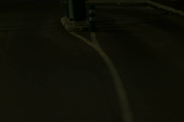 A solitary person is walking cautiously down a dimly lit, dark street during the late hours of the night, surrounded by shadows