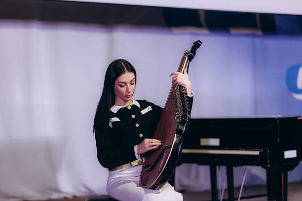 A talented woman performs using a traditional string instrument, creating soothing music during an engaging stage performance. The scene captures the dedication and harmony involved in a live musical act.