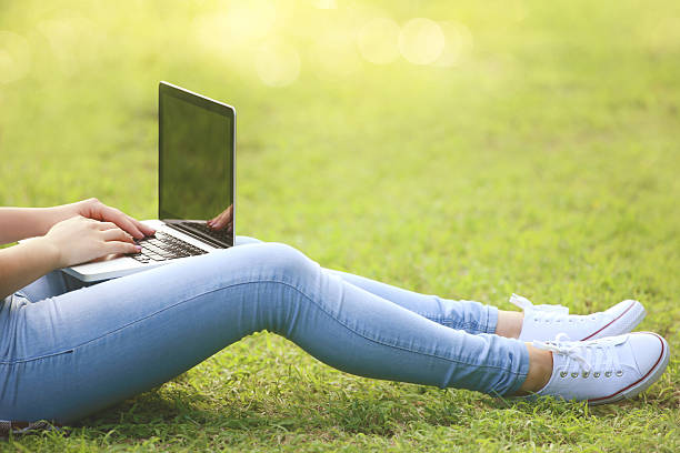istock Young girl with laptop computer sitting on the grass in park 2204584556