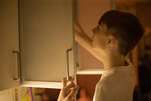 A young boy enthusiastically reaching into the kitchen cabinet for snacks