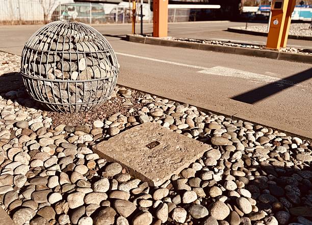 A Visually Striking Artistic Stone Ball and Pebble Display Set in an Urban Environment. In an innovative urban environment, a striking stone ball sculpture is elegantly nestled among smooth pebbles