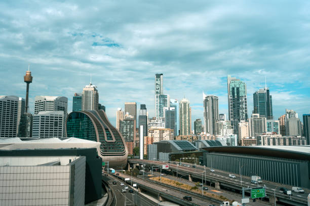 Modern Sydney skyline with towering skyscrapers, cloudy sky, and busy urban roads. The view showcases architectural diversity and dynamic urban life in Australia.