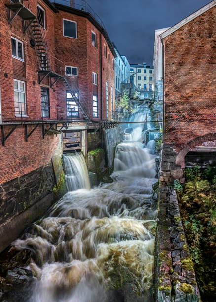 istock powerful rushing waterfall surrounded by industrial brick buildings.. 2204594148