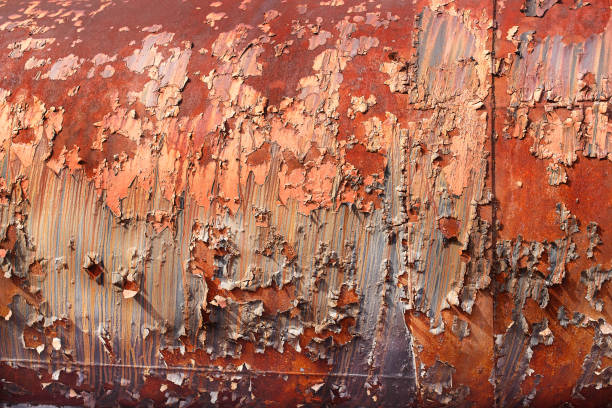 Close-up of deteriorating metal surface showing extensive rust and peeling paint at the historic Bethlehem Steel site in Pennsylvania. The surface displays multiple layers of orange-red paint flaking away to reveal the underlying metal structure. Years of exposure to elements have created a textured pattern of corrosion and decay on this industrial landmark.