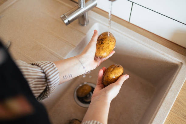 Unrecognisable female hands washing potatoes in a kitchen sink, removing dirt before peeling and cooking
