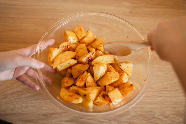 The close-up view of woman’s hands mixing seasoning potatoes before frying