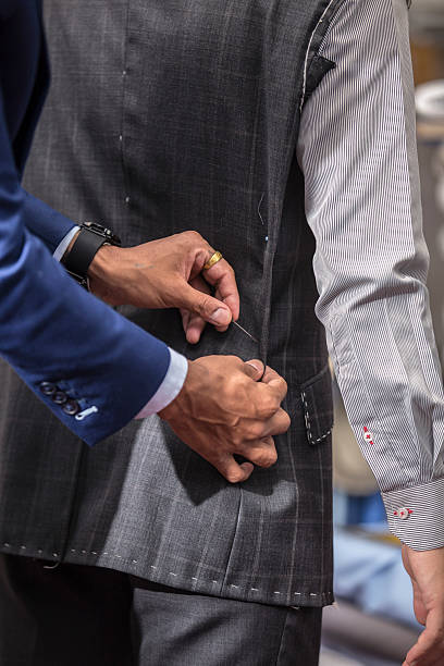 istock Close-up of bespoke tailor adjusting a dark gray pinstripe suit jacket on a client. Dressed in a blue suit, carefully buttons the jacket, showcasing the precision and craftsmanship 2204596844