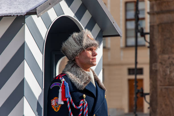 02-21-2025, Prague, Portrait of a Czech guard wearing winter uniform with fur hat and collar, standing in front of a striped sentry box at Prague Castle on a cold winter day