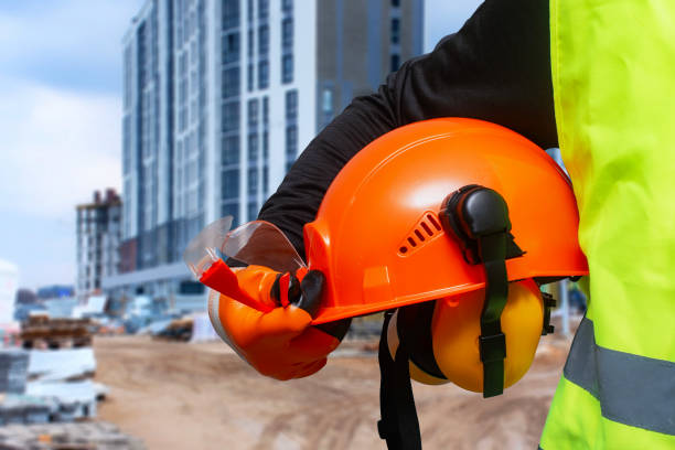 istock Construction worker in a high-visibility vest holding an orange safety helmet and protective gear at a building site. 2204598517