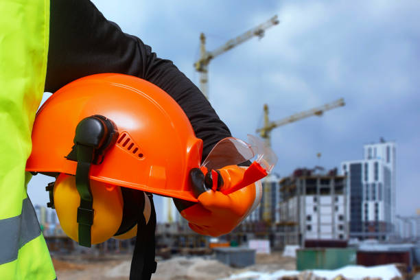 istock Construction worker in a high-visibility vest holding an orange safety helmet and protective gear at a building site. 2204598518