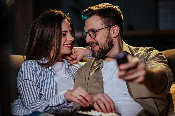 istock Happy couple watching tv and eating popcorn on sofa at night 2204599403