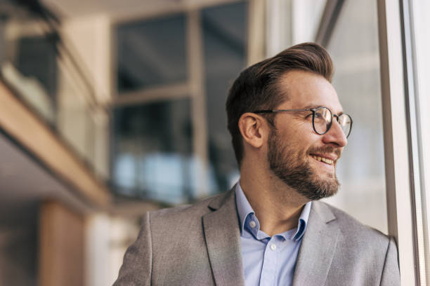 istock Businessman smiling and looking out the window in modern office 2204611907