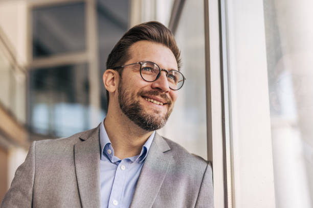 istock Businessman smiling and looking out the window in office 2204611922