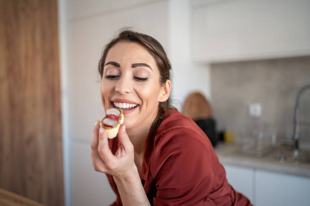 istock Young woman enjoying delicious canape in modern kitchen 2204611932