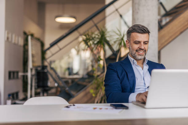 istock Smiling businessman working on laptop in modern office 2204611936