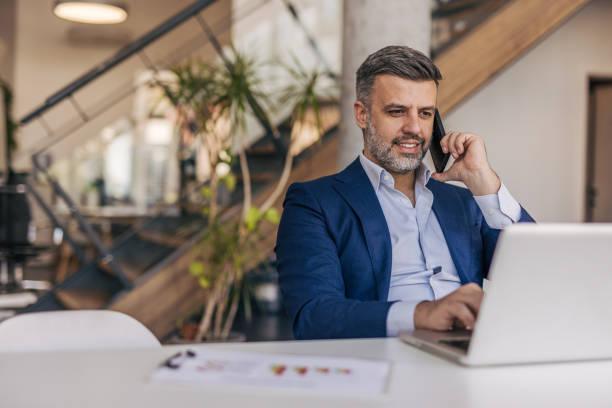 istock Businessman working on laptop and talking on phone in modern office 2204612021
