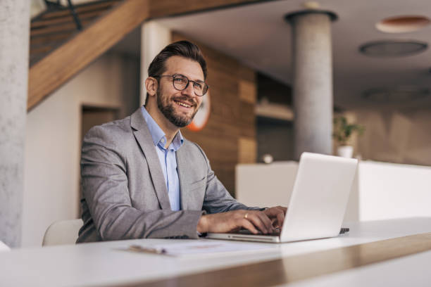 istock Businessman working on laptop in modern office and smiling 2204613213