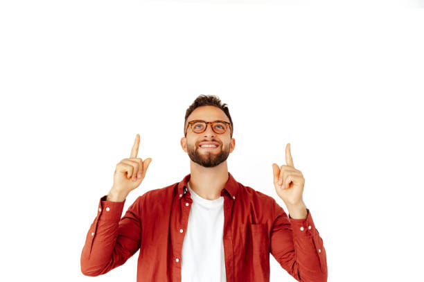 Happy handsome stylish caucasian or arabian man dressed in a red shirt and with glasses, standing on isolated white background and points up with fingers, shows copy space and advertising, smiling stock photo