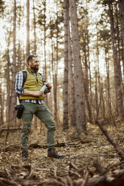 istock A middle-aged male photographer drinks water while taking a break and taking nature photos surrounded by a beautiful pine forest. 2204623108